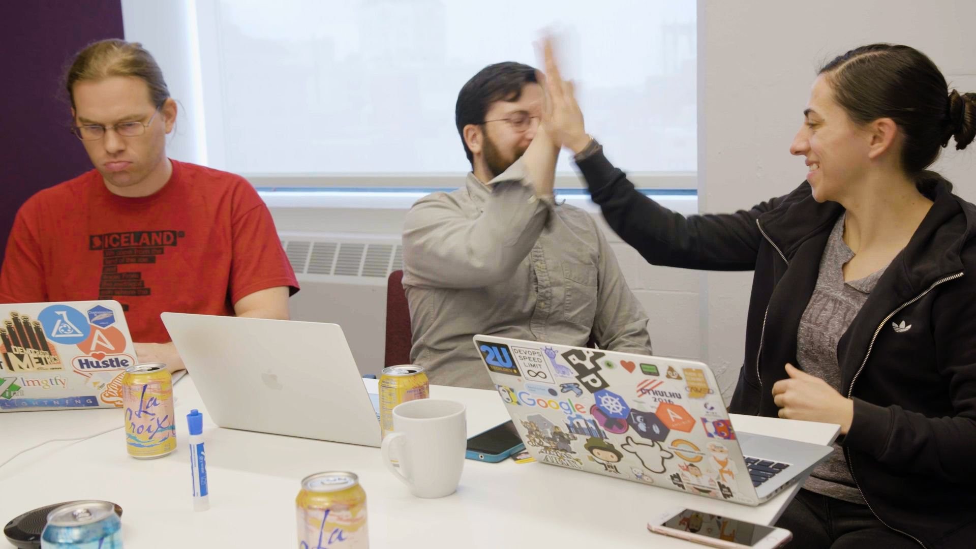 Colleagues high five each other next to laptops with lots of stickers on them