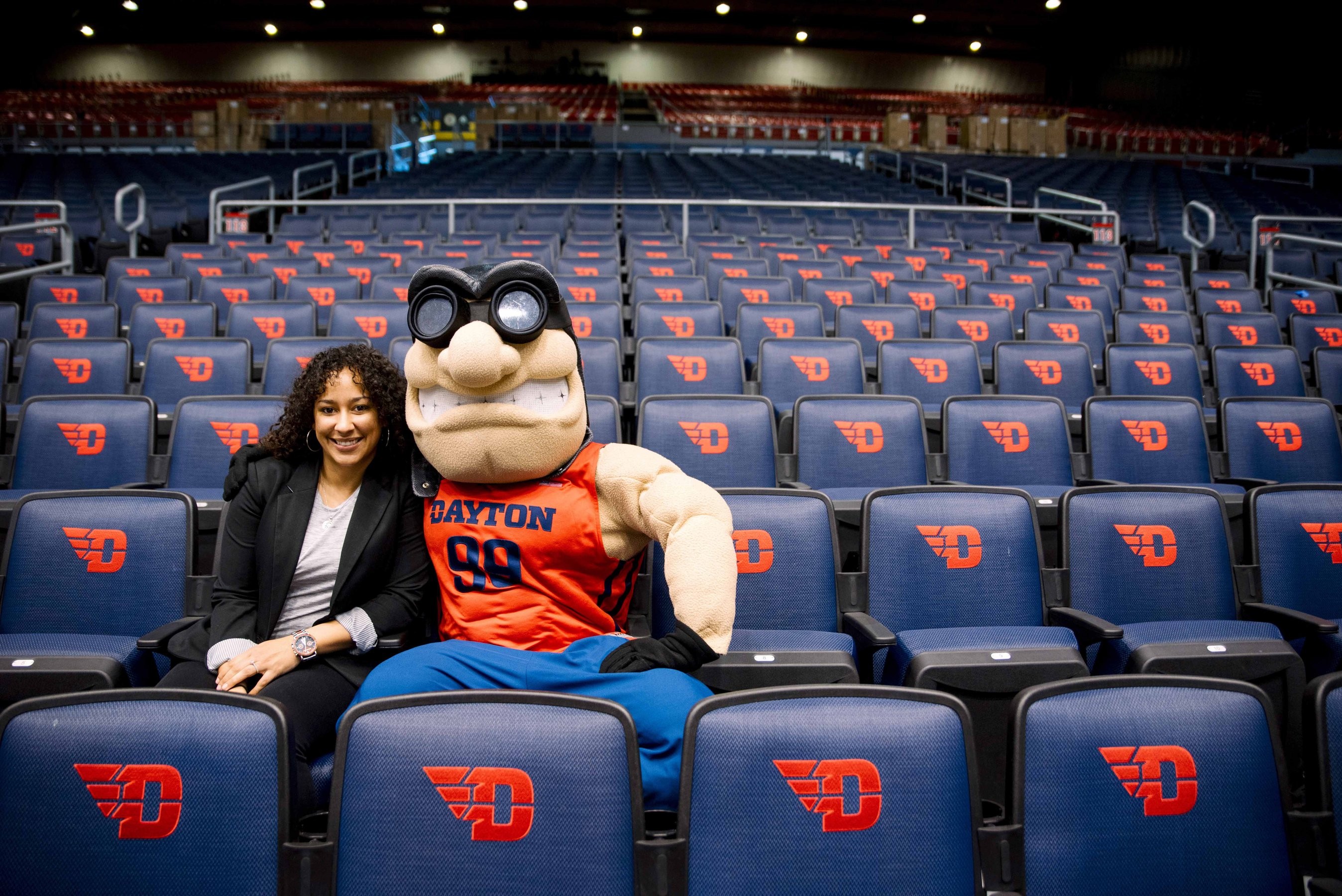 University of Dayton's mascot, Rudy Flyer, poses for a seated photo with a student in UD Arena