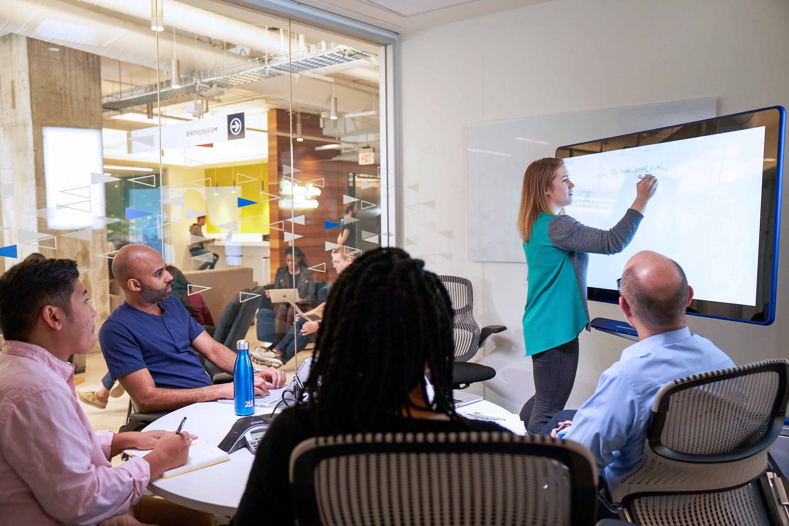 Woman writing on a digital whiteboard addresses colleagues during a meeting