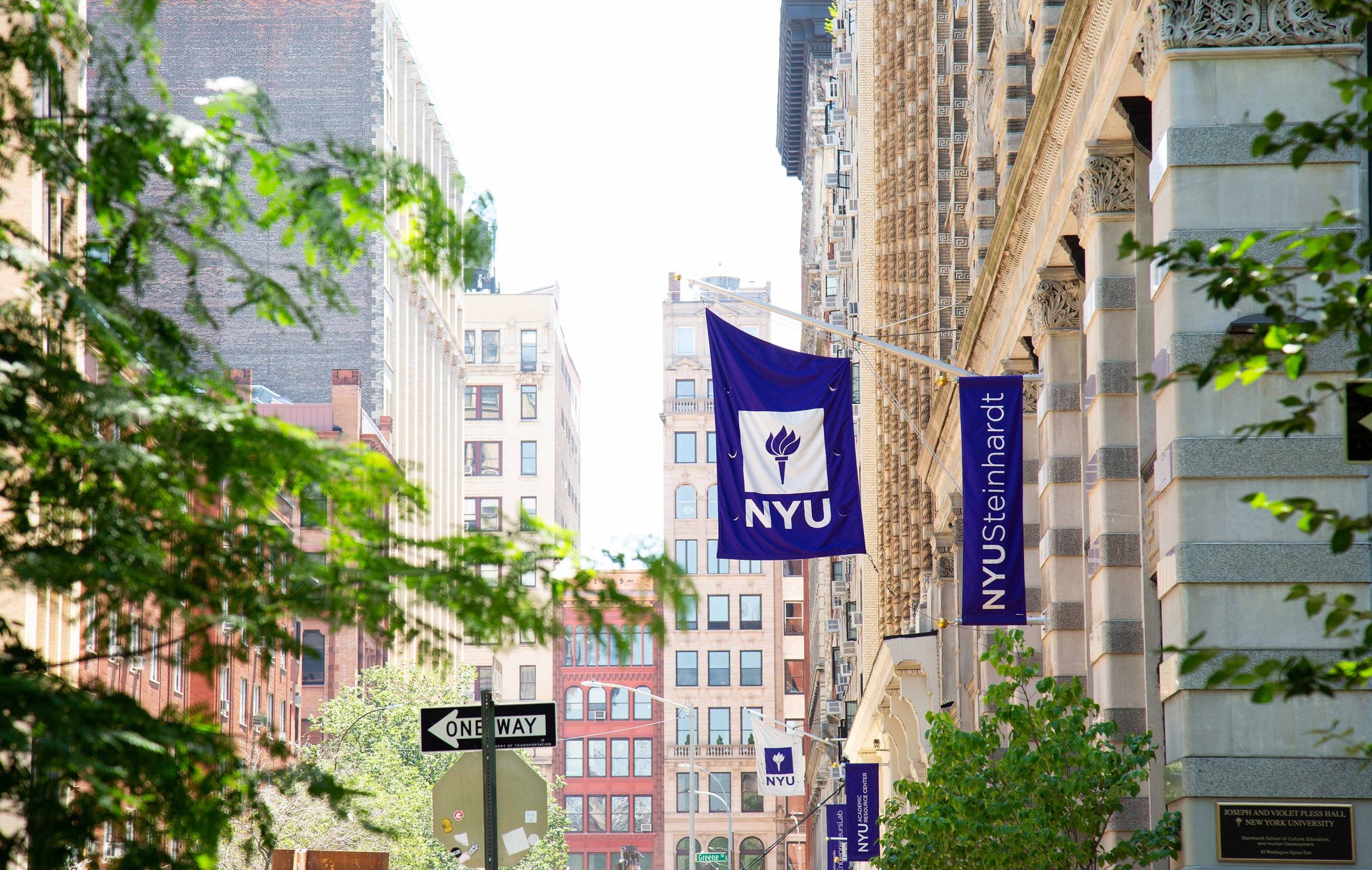 NYU Steinhardt campus flags hang over a sidewalk between campus buildings