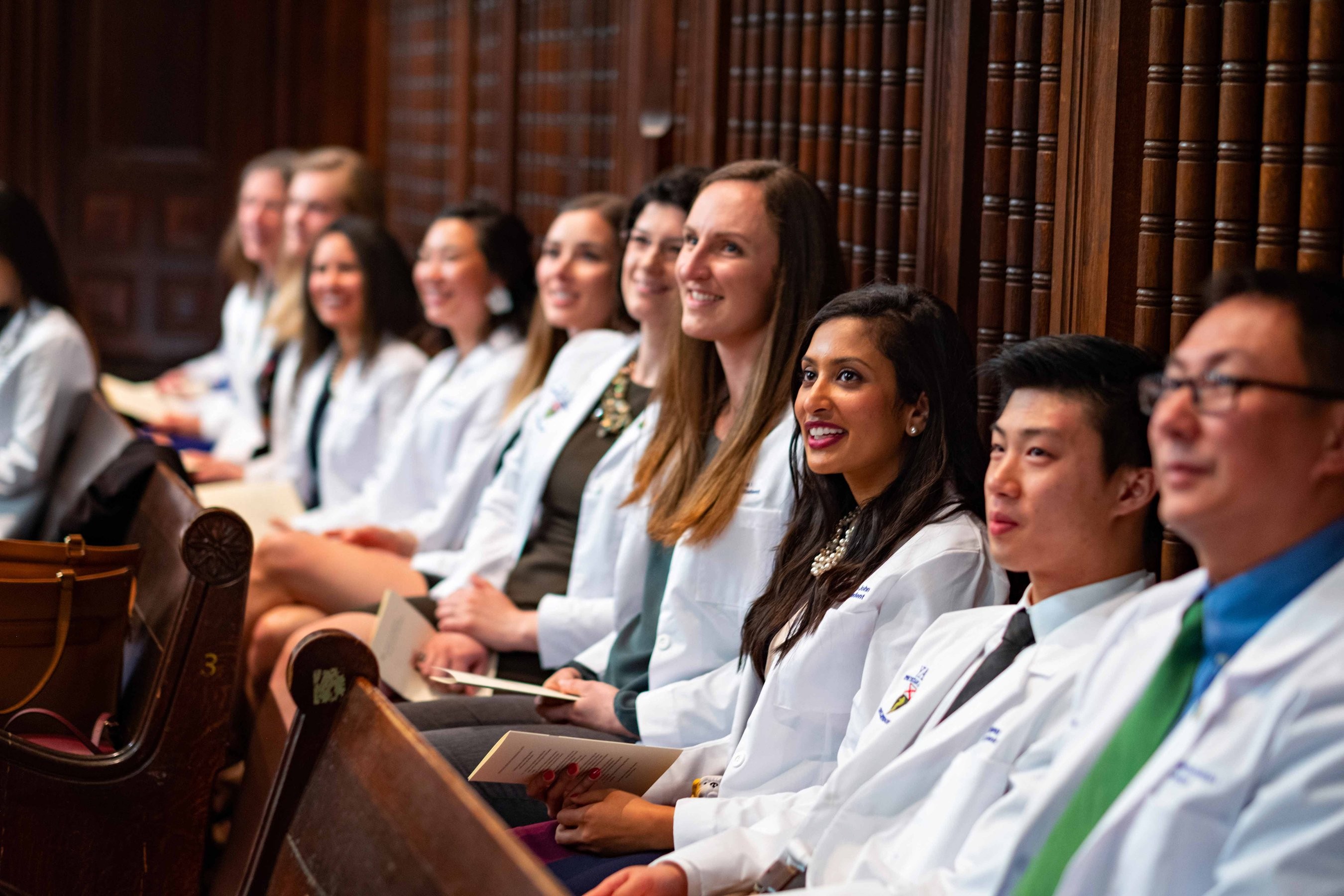Students smiling and sitting at the white coat ceremony at medical school graduation